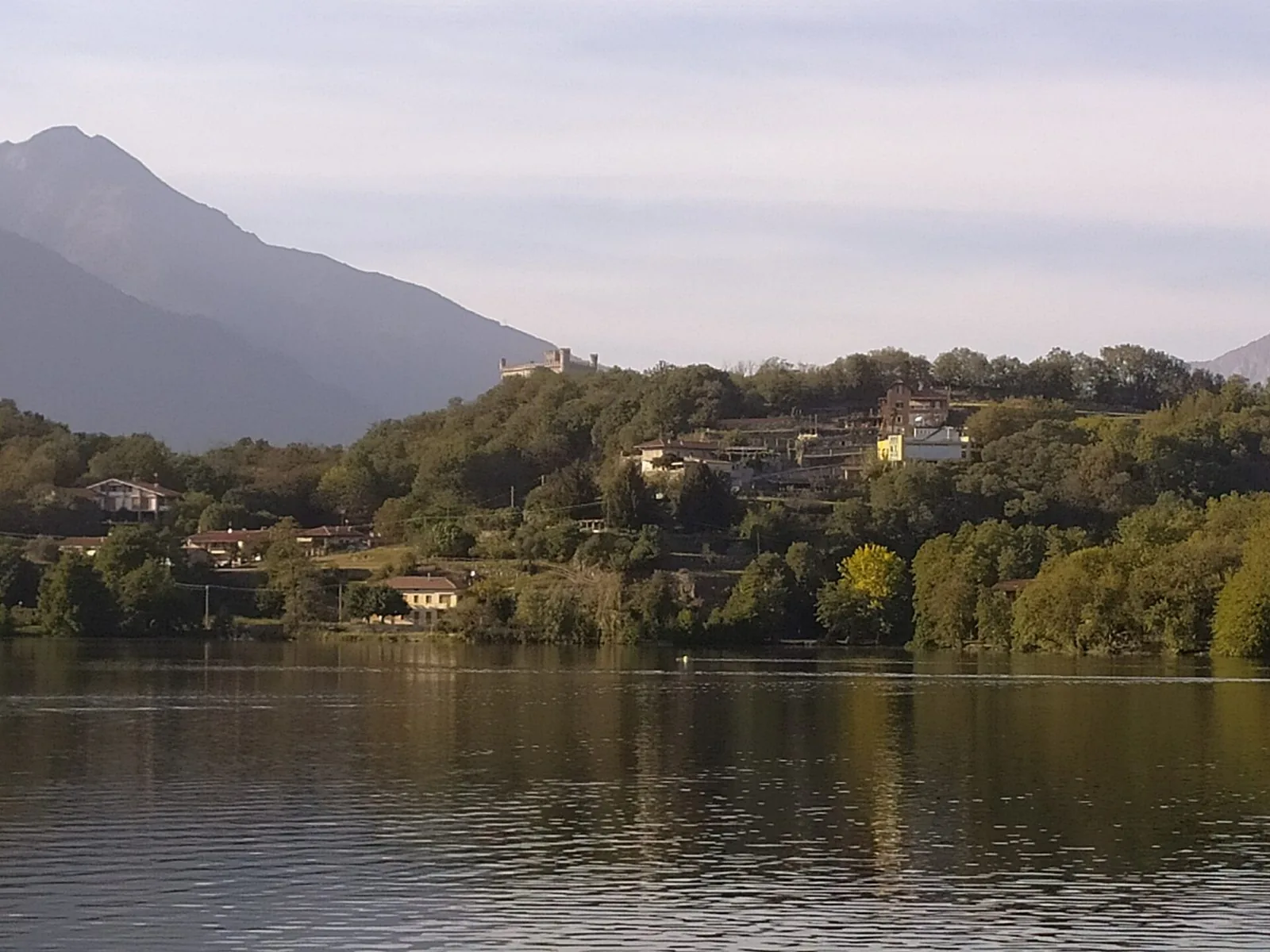 Le case di Montalto Dora sulla collina boscosa affacciata sul lago, con il castello in alto sullo sfondo delle montagne
