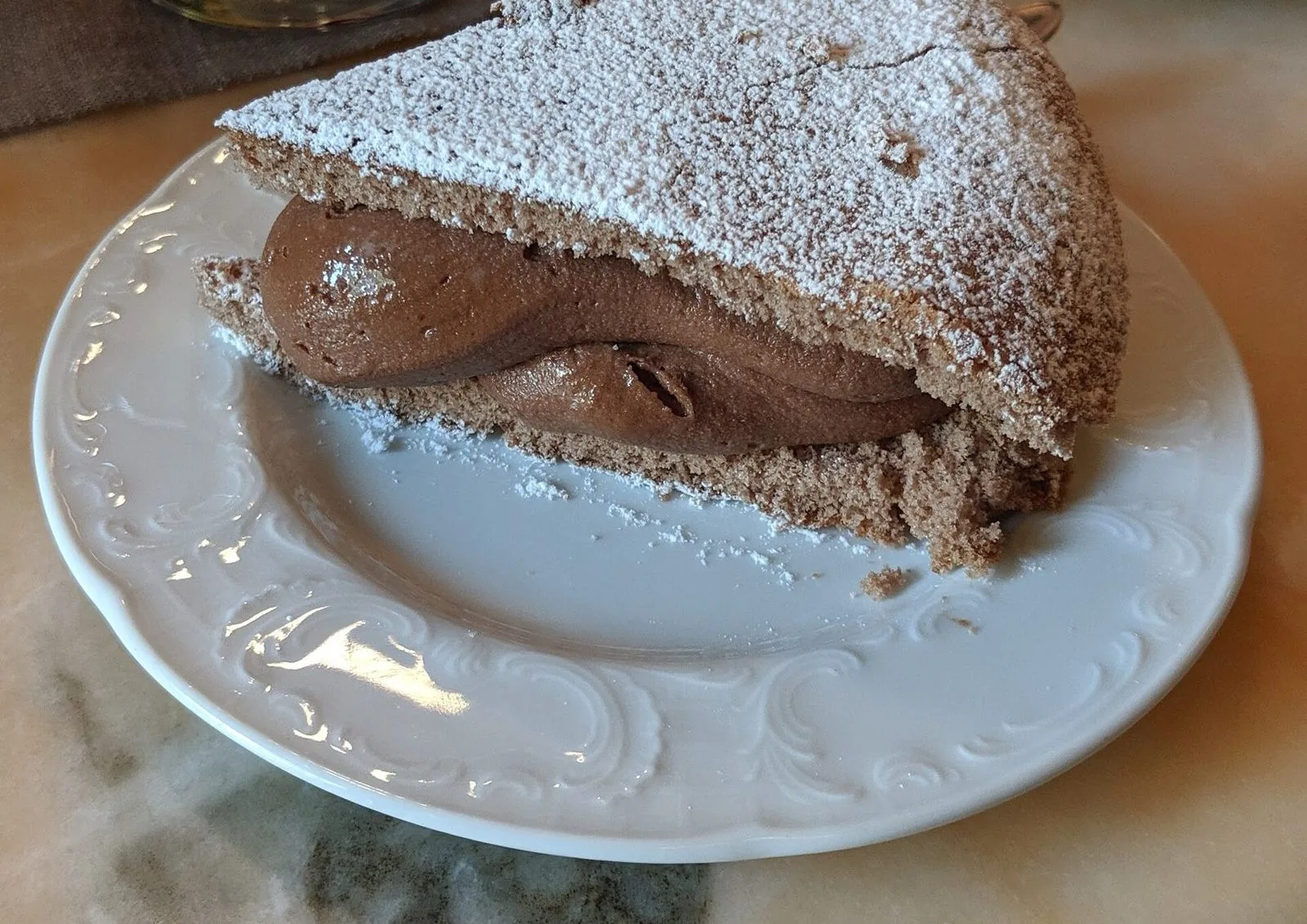 Fetta di Torta 900 di Ivrea con pan di Spagna al cacao, crema al cioccolato e zucchero a velo su un piatto bianco